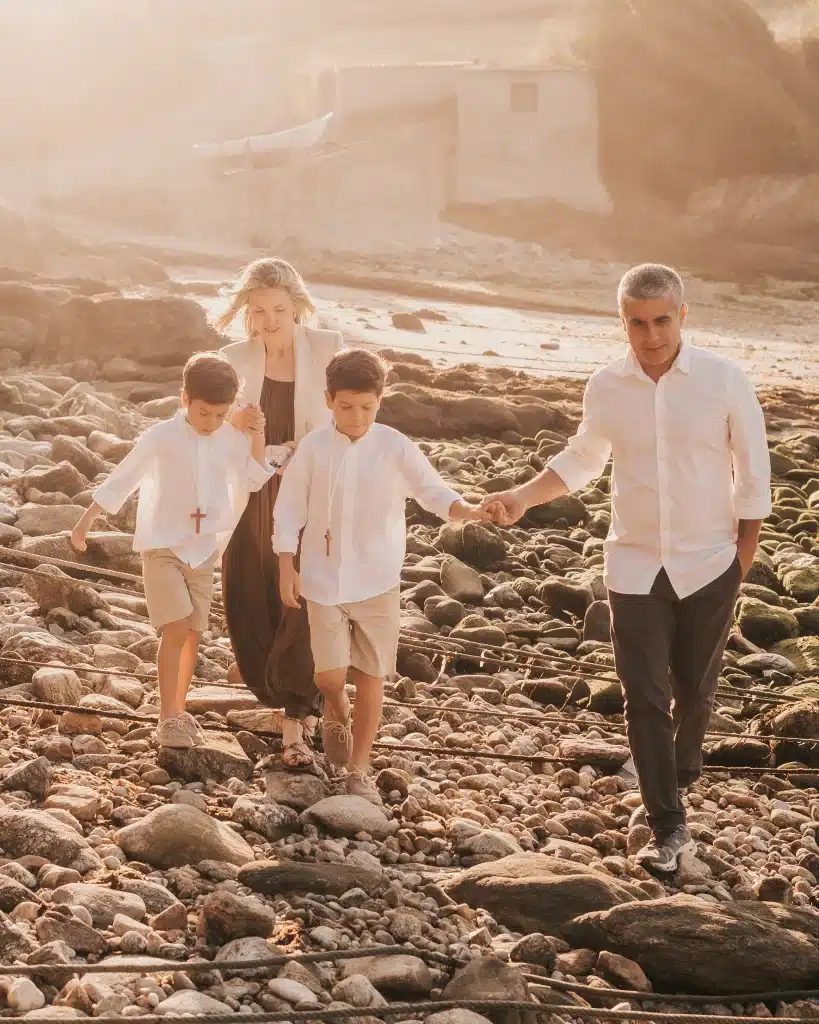 Fotografia de dos niños de comunión paseando por la playa con sus papás.