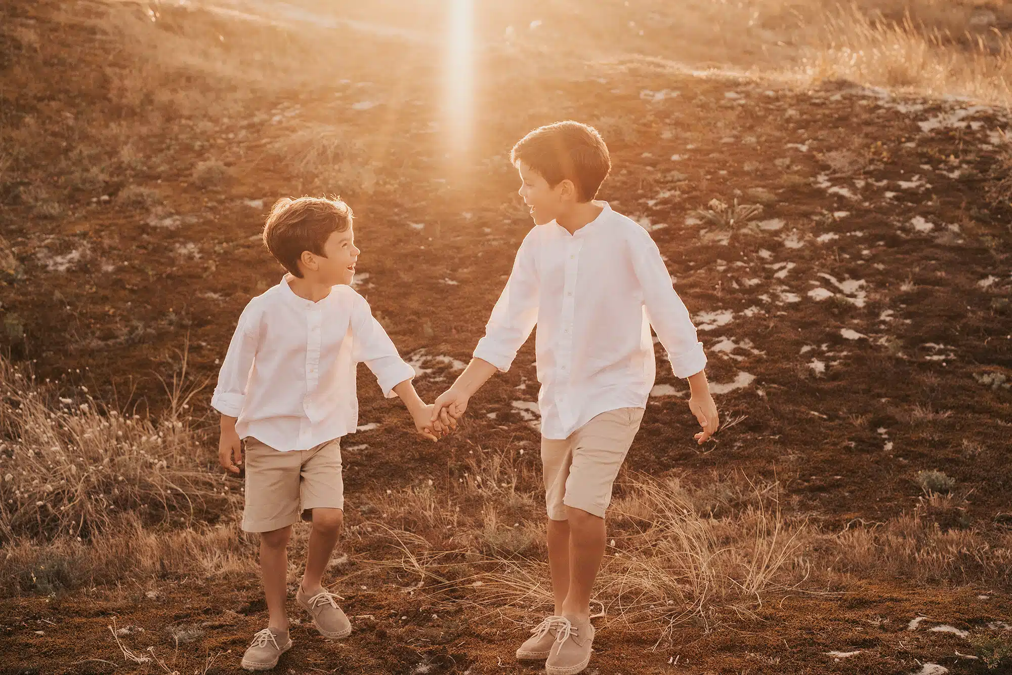 Fotógrafo de comunión. Hermanos de comunión riendo a carcajadas en dunas de arena.